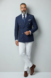 Man wearing navy double-breasted suit set with white trousers and brown shoes.